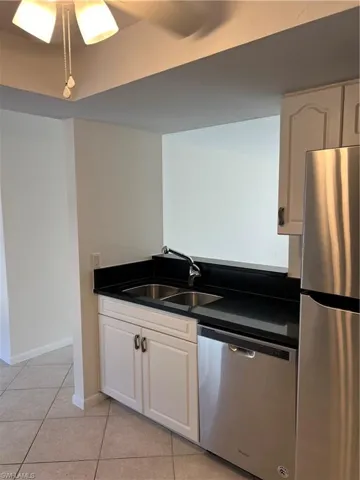 Kitchen with dishwasher, sink, refrigerator, white cabinets, and light tile patterned flooring