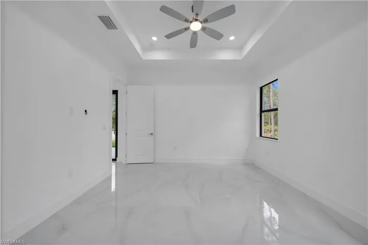 Spare room with light marble finish floors, a raised ceiling, recessed lighting, and ceiling fan