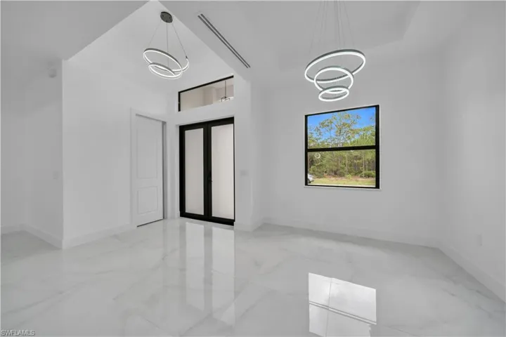 Empty room featuring light marble finish flooring, a towering ceiling, french doors, and a chandelier
