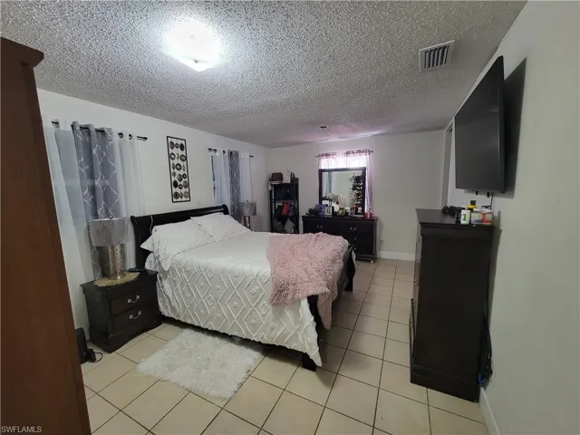 Bedroom featuring light tile patterned floors, visible vents, a textured ceiling, and baseboards