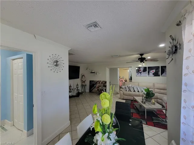 Living room with a textured ceiling, light tile patterned floors, ceiling fan, and visible vents