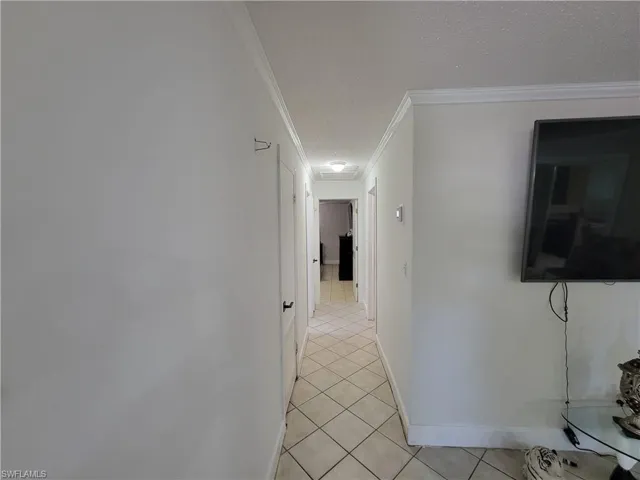Corridor featuring crown molding, light tile patterned floors, baseboards, and a textured ceiling