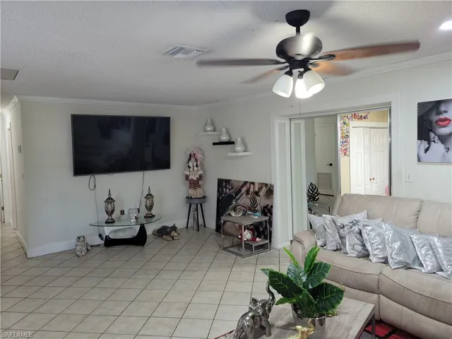 Living area with visible vents, ceiling fan, a textured ceiling, crown molding, and light tile patterned flooring