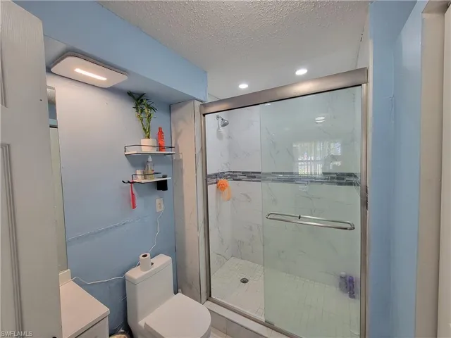 Bathroom with recessed lighting, a textured ceiling, toilet, and a marble finish shower