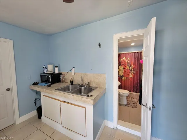 Kitchen featuring a sink, light tile patterned floors, black microwave, and light countertops