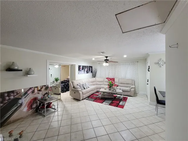 Living area featuring baseboards, light tile patterned floors, a textured ceiling, crown molding, and visible vents