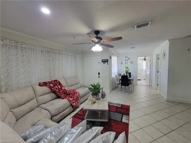 Living room featuring visible vents, light tile patterned floors, ornamental molding, a ceiling fan, and a textured ceiling