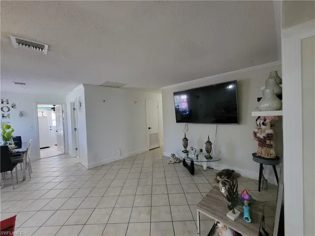 Living room with a textured ceiling, light tile patterned floors, ornamental molding, and visible vents