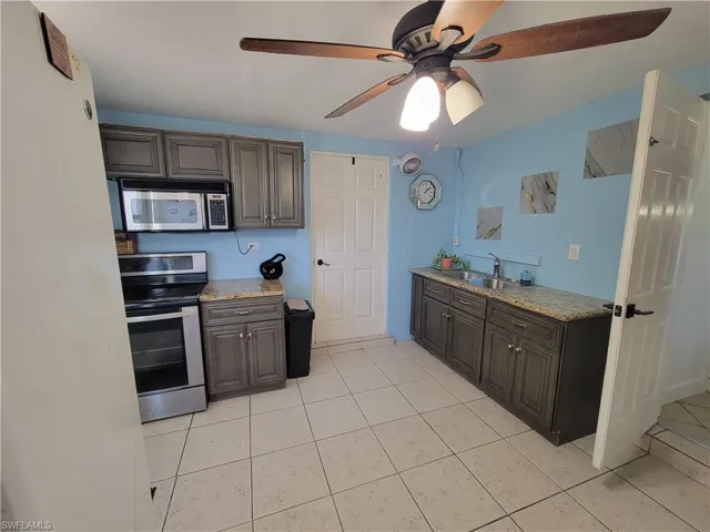 Kitchen with ceiling fan, a sink, light stone counters, and appliances with stainless steel finishes