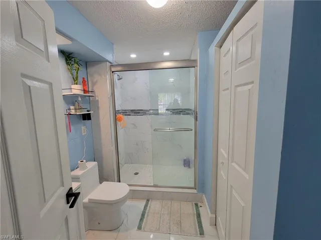Full bath with a marble finish shower, toilet, marble finish floor, and a textured ceiling