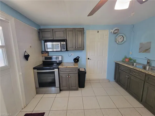 Kitchen with a sink, light tile patterned floors, appliances with stainless steel finishes, and a ceiling fan