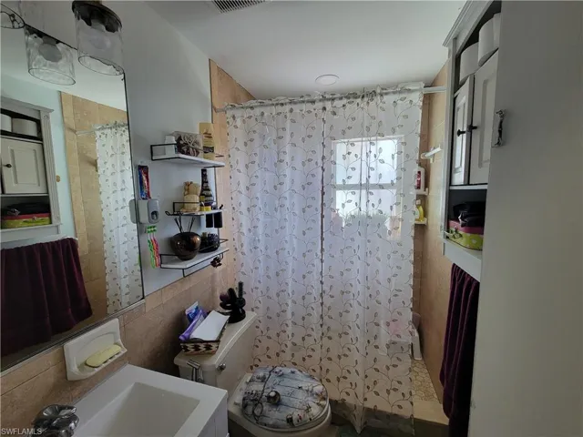 Full bathroom featuring a shower with curtain, visible vents, and tile walls