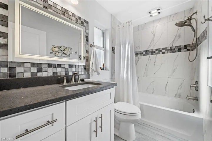 Luxurious Primary Ensuite - a full bathroom with vanity, shower / tub combo boasting brand new tile, double shower heads, a stylish modern new shower curtain, and decorative backsplash. And what a modern beautiful mirror!!