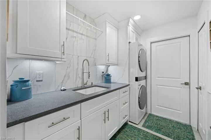 What a well organized Laundry room  featuring stacked washer and clothes dryer, cabinet space, dark tile patterned flooring, and recessed lighting. Plus hanging space!