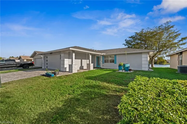 Rear view of house with a yard, stucco siding, driveway, and an attached garage