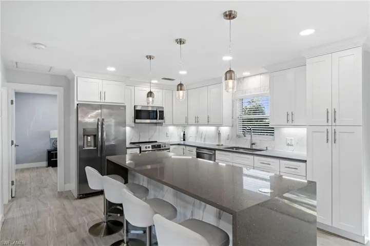 Kitchen featuring dark stone countertops, stainless steel appliances, a breakfast bar area, and white cabinets