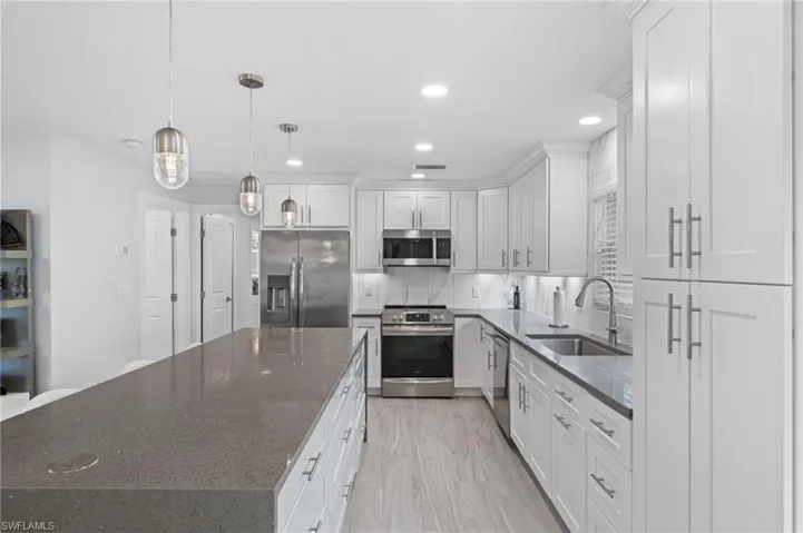 Kitchen featuring dark stone countertops, stainless steel appliances, a spacious island, and white cabinets