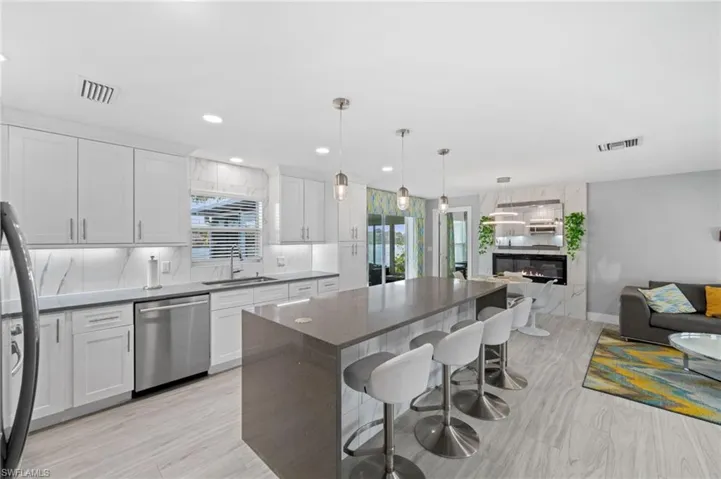 Kitchen with a kitchen bar, dark stone countertops, open floor plan, stainless steel dishwasher, and a premium fireplace
