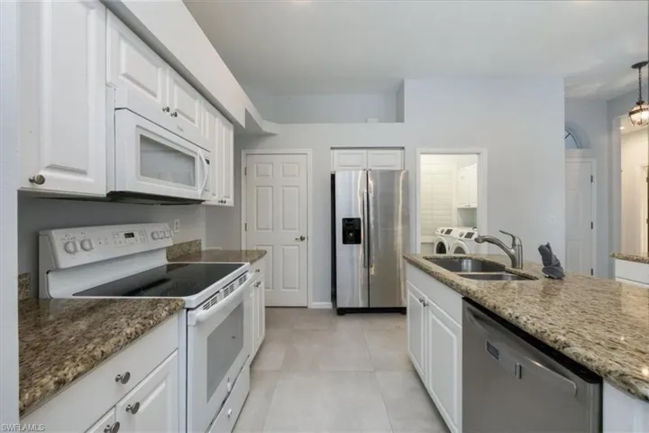 Kitchen featuring appliances with stainless steel finishes, white cabinets, and light stone counters