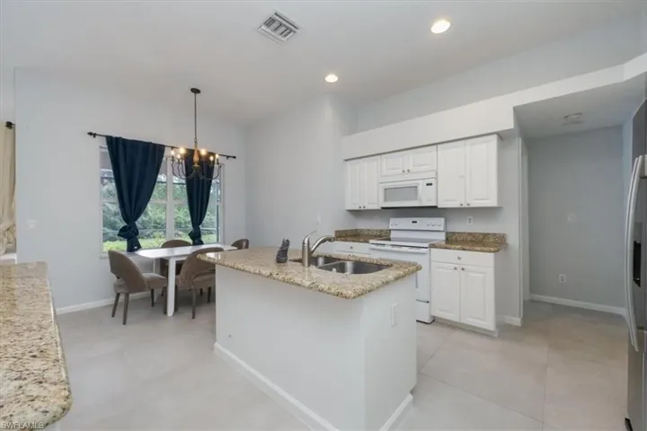 Kitchen with a chandelier, white appliances, an island with sink, light stone countertops, and decorative light fixtures
