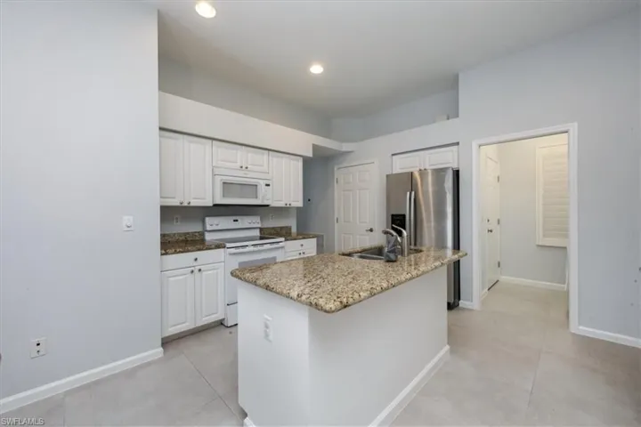 Kitchen featuring white appliances, white cabinetry, an island with sink, dark stone counters, and recessed lighting