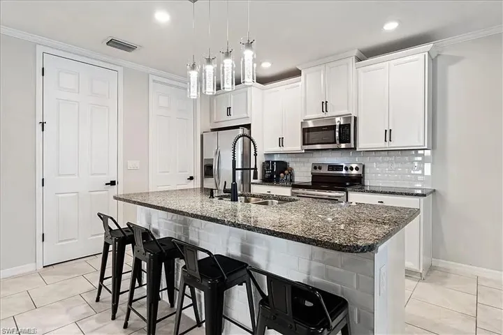 Kitchen featuring ornamental molding, dark stone countertops, a breakfast bar, stainless steel appliances, and white cabinetry