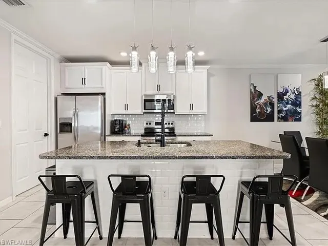 Kitchen featuring light tile patterned floors, appliances with stainless steel finishes, ornamental molding, a kitchen breakfast bar, and decorative backsplash