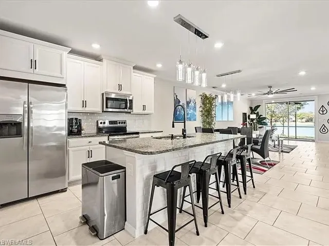 Kitchen with appliances with stainless steel finishes, ceiling fan, dark stone countertops, a kitchen bar, and a kitchen island with sink