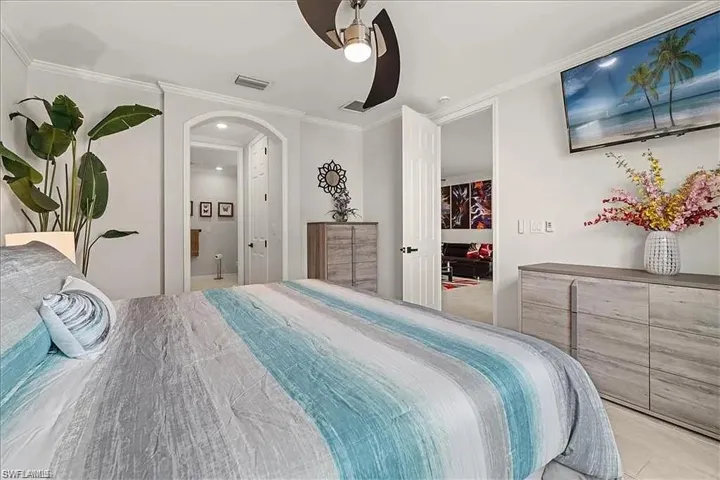 Bedroom with ornamental molding, a ceiling fan, connected bathroom, and arched walkways