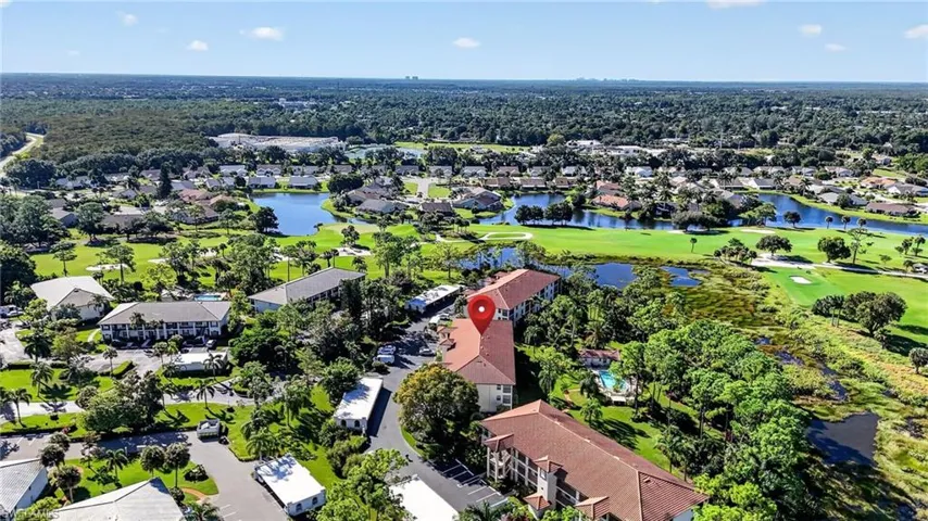 Aerial perspective featuring multi-story residential buildings, tile roofing, paved parking areas, and mature landscaping