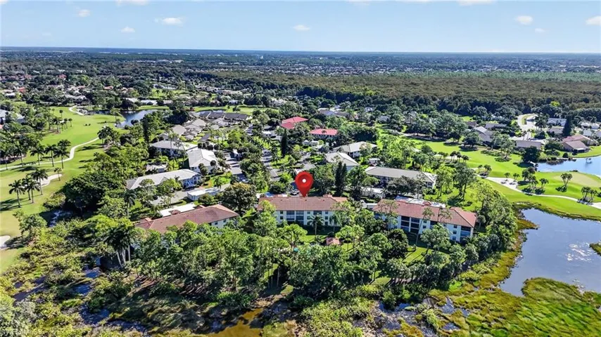 Aerial perspective of a multi-story residential building featuring low-pitch roofing, expansive grounds, mature landscaping, and proximity to water and golf course fairways