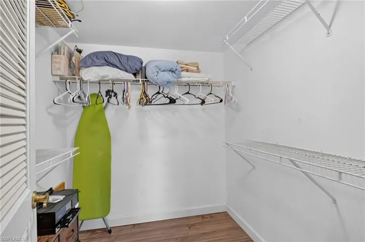 Storage space featuring wood-finish flooring, white louvered door, and multi-tier wire shelving