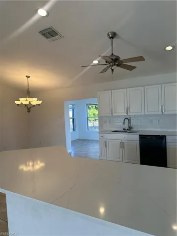 Kitchen featuring white cabinets, dishwashing machine, backsplash, light stone countertops, and recessed lighting