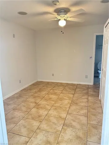 Empty room featuring light tile patterned floors, a ceiling fan, and a smoke detector