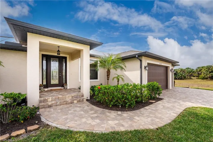 Property entrance with a garage, stucco siding, and decorative driveway
