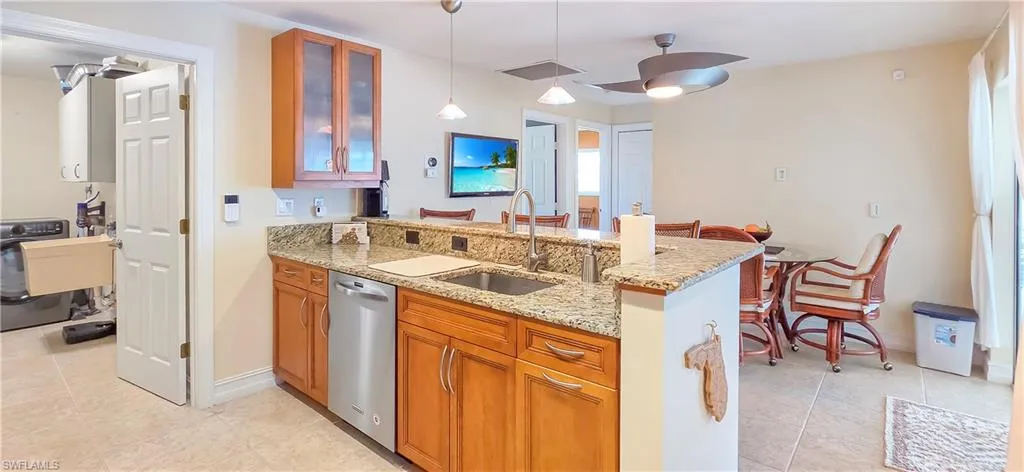 Kitchen featuring granite countertops, wood cabinetry, stainless steel dishwasher, and a double basin sink with a high-arc faucet