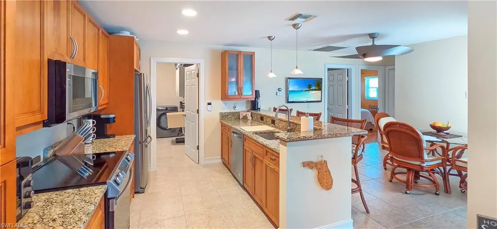Open-concept kitchen featuring wood cabinetry, granite countertops, stainless steel appliances, and a breakfast bar with pendant lighting