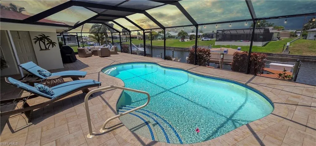 Screened lanai featuring a freeform swimming pool with integrated steps, surrounded by a paver deck