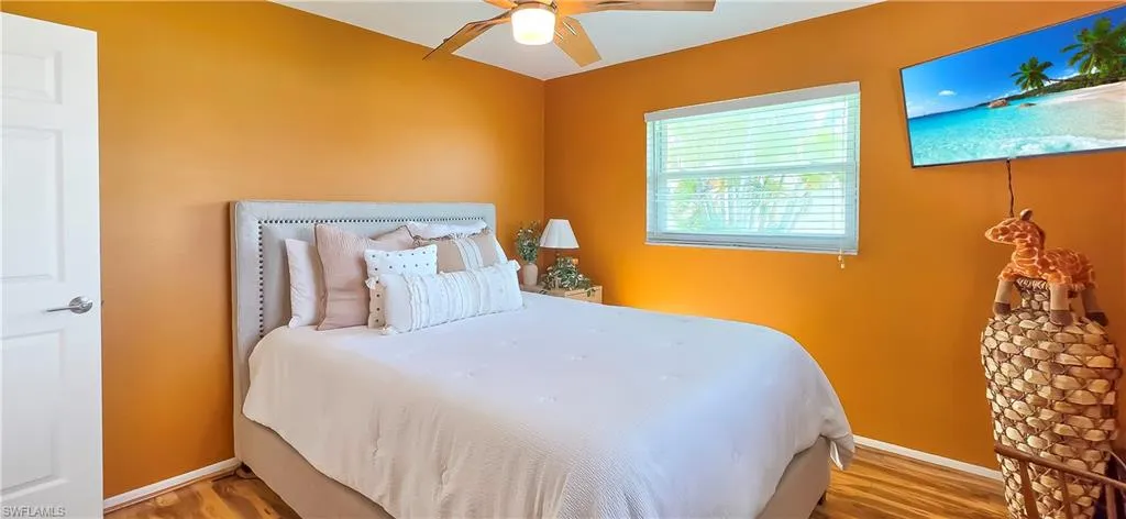Room featuring a ceiling fan with light fixture, window with horizontal blinds, wood-finish flooring, and a white interior door