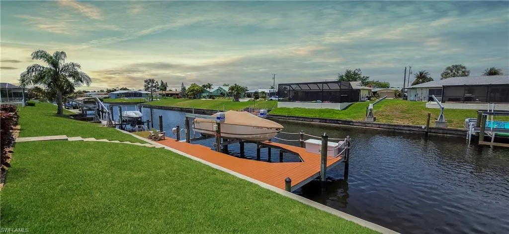 Waterfront property featuring a private boat dock with lift, lush green lawn, and mature palm trees