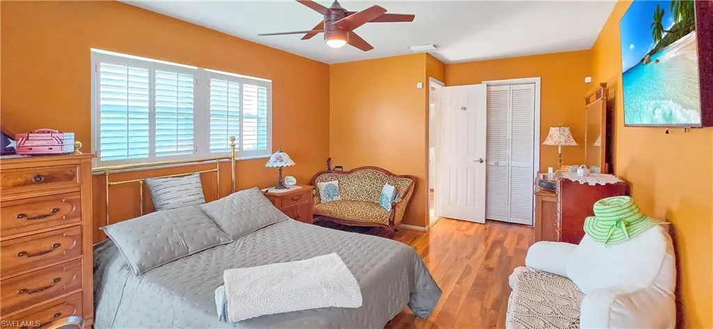 Bedroom featuring wood-finish flooring, white plantation shutters, a ceiling fan with integrated lighting, and a closet with bifold doors