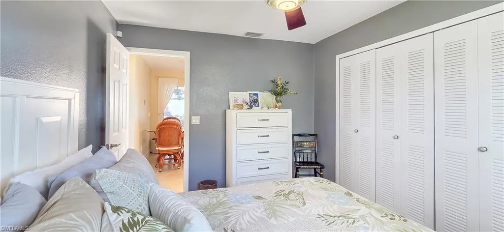 Room with gray walls and a ceiling fan featuring white louvered bifold closet doors, a white paneled headboard, and wood-finish flooring visible through an open doorway