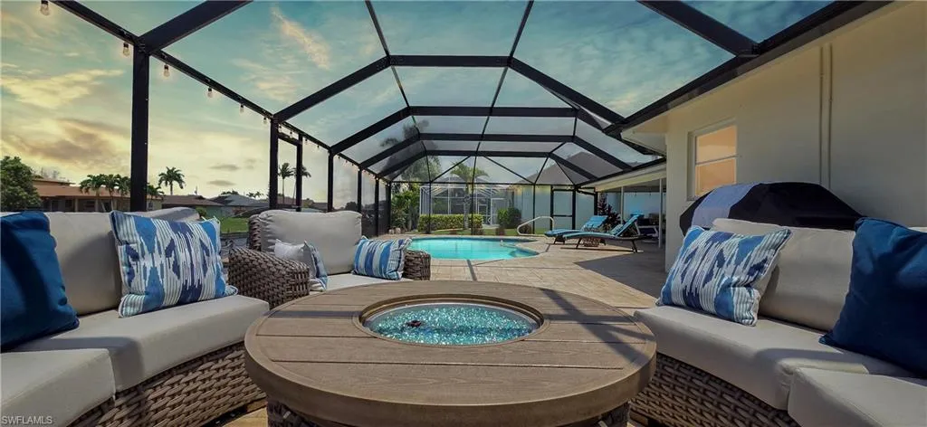 Screened lanai featuring a built-in fire pit, spacious paver patio, in-ground swimming pool, and string lighting