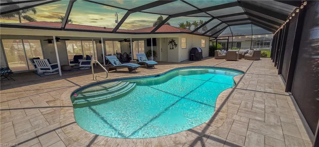 Screened pool area featuring a freeform swimming pool with steps, paver patio, and covered lanai