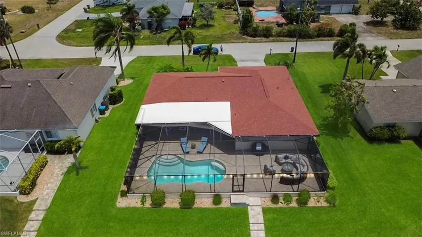 Expansive screened pool enclosure featuring a curved swimming pool, paved patio, and perimeter landscaping