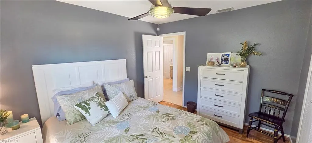 Hardwood-finish flooring, a white paneled headboard, a ceiling fan with light fixture, and a white six-drawer dresser