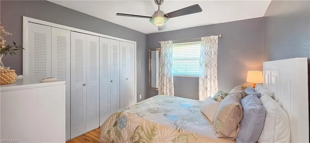 Bedroom featuring wood-finish flooring, a ceiling fan with integrated lighting, a window with blinds and curtain rod, and louvered bi-fold closet doors