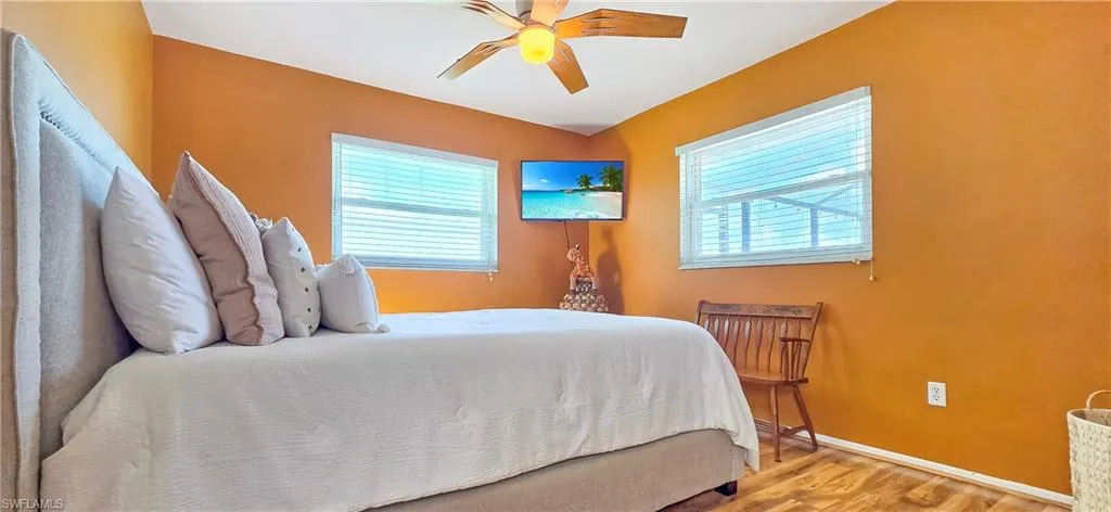 Bedroom featuring wood-finish flooring, two windows with horizontal blinds, and a built-in ceiling fan with light fixture