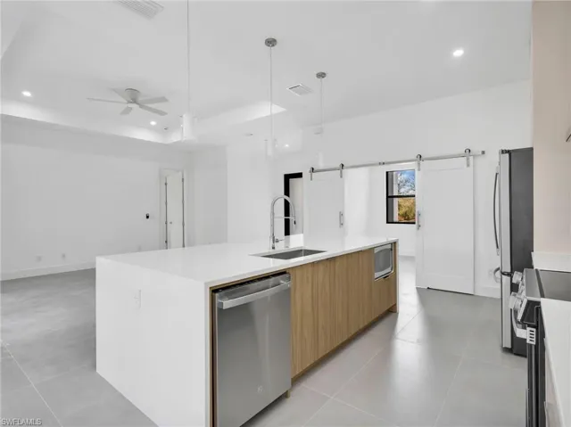 Kitchen featuring a barn door, a kitchen island with sink, light stone countertops, modern cabinets, and stainless steel appliances