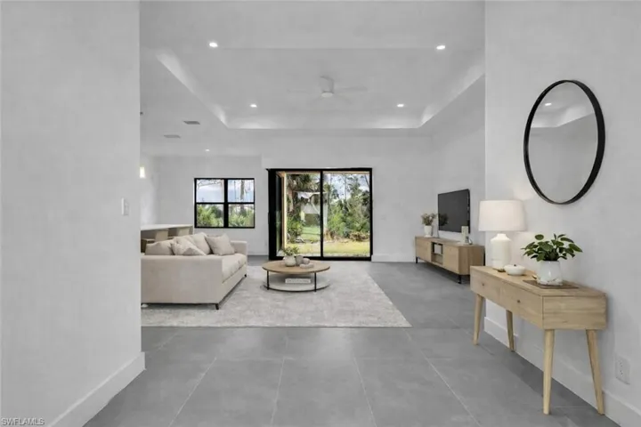 Living area featuring a ceiling fan, concrete floors, a raised ceiling, and recessed lighting. This photo was digitally staged.